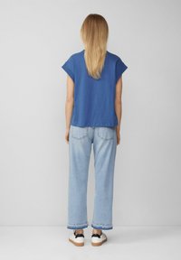 Blaue Kurzarmbluse mit lockerer Passform, kombiniert mit hellblauen weiten Jeans, die gekrempelte Säume und bequeme Sneaker aufweisen.
