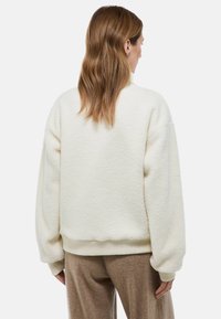Sweatshirt en polaire crémeuse, fluffy, avec des épaules tombantes, des poignets et un ourlet côtelés, et une coupe décontractée. La vue arrière montre une texture douce.