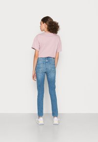 T-shirt rosa de manga curta combinada com jeans justos de tom azul claro. Os jeans têm bolsos traseiros e um desvanecimento subtil. O calçado inclui ténis chunky.