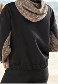 Black sweatshirt with a patterned beige hood and cuffs featuring repeating text. Soft fabric, relaxed design, elastic waistband.