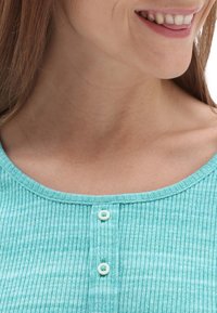 Haut côtelé couleur bleu sarcelle clair avec un col arrondi, deux boutons au centre, et une texture douce avec de subtiles rayures horizontales.