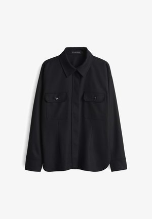 Black shirt made of smooth fabric, featuring a pointed collar, two front pockets with button flaps, and long sleeves with buttoned cuffs.