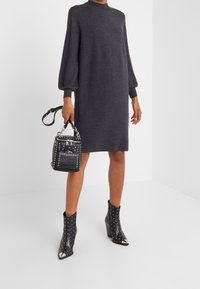 Robe en maille gris foncé avec manches ballon, associée à des bottines noires à clous et un petit sac à main clouté.