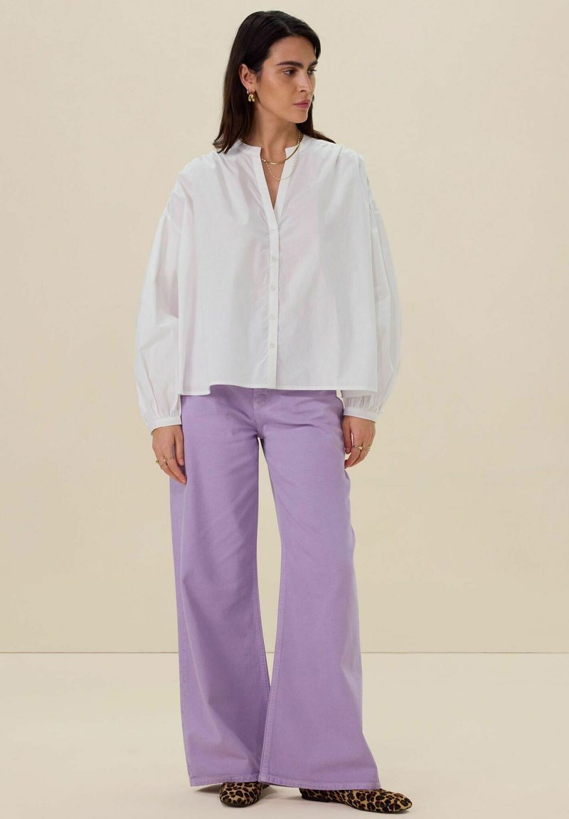 Witte button-up shirt met brede mouwen, gecombineerd met hoge lichtpaarse wijde broek en schoenen met dierenprint. Gladde stof, ontspannen pasvorm.