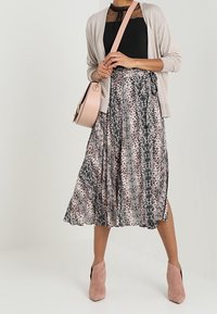 Lett, knælange nederdel med et mønster af sort, grå og lyserød slangeprint; parret med en sort top og en blød beige cardigan. Lyserøde hæleboots.