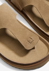 Bruna mockaskor med tongsdesign, som har en texturerad ovandel, vadderat innersula och en subtil sömdetalj längs kanten.