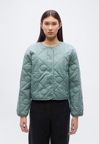 Πράσινο μπουφάν σε αποχρώσεις μέντας με καπιτονέ σχέδιο, στρογγυλή λαιμόκοψη, κουμπιά με κλιπ και φαρδιά εφαρμογή. Διαθέτει κυκλικό καπιτονέ μοτίβο και ελαστικές μανσέτες.