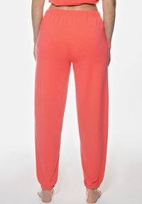 Korallfärgade joggers i mjukt tyg, med elastisk midja, fickor i sidan och smalnande manschetter vid anklarna.