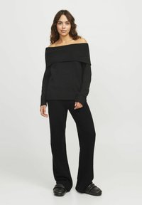 Zwarte off-the-shoulder trui met ribbelstructuur, gecombineerd met zwarte wijd-uitlopende broek, gemaakt van zachte stof en met een relaxte pasvorm.