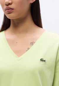 T-shirt col en V en coton vert clair avec manches courtes et petit logo crocodile brodé sur la poitrine gauche. Texture lisse.