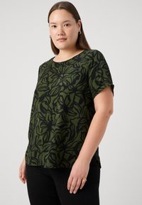 Kortärmad topp i mörkgrön med ett svart blommönster. Tillverkad av mjukt tyg med en avslappnad passform och rund halsringning.