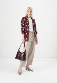 Camicia a fiori borgogna, camicia bianca, pantaloni beige e scarpe con tacco grigie; porta una borsa in pelle rossa scura con dettaglio in fibbia.