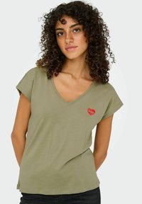 Olivengrøn kortærmet V-hals t-shirt med et rødt læbeprint på venstre brystområde. Blødt stof med en afslappet pasform.