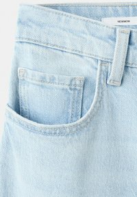 Jean en denim bleu clair avec poche avant, passants pour ceinture et étiquette "NEWMOM" visible sur la ceinture intérieure.