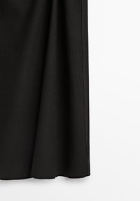 Jupe noire suspendue, montrant un tissu lisse et des coutures discrètes le long du bord sur un fond blanc.