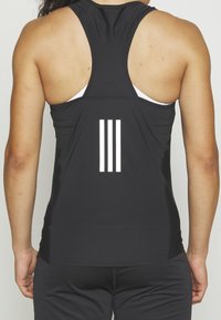 Débardeur de sport noir avec un dos nageur, présentant trois bandes horizontales blanches à l'arrière, fabriqué en tissu texturé.