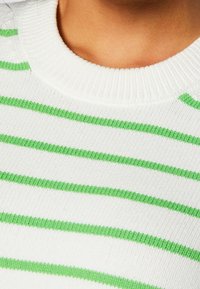 Biały sweter dziany w zielone poziome paski, z prążkowanym, okrągłym dekoltem i miękką fakturą. Widok z bliska podkreśla wzór i kontrast kolorów.