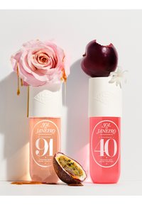 Twee parfumflesjes met witte doppen. Het linker flesje is roze met een roos erop; het rechter flesje is felroze met een paarse vrucht ernaast.