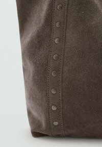 Brązowa torba z zamszu o gładkiej fakturze, z ozdobnym rzędem okrągłych metalowych ćwieków po jednej stronie. Prosty, pionowy design.