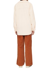 Lichtroze corduroy overshirt met een kraag, lange mouwen en een gebogen zoom, gecombineerd met roestkleurige wijde broek en witte schoenen.