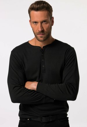Chemise noire à manches longues avec une texture côtelée horizontale, dotée d'un col rond et d'une patte de boutonnage à cinq boutons. Coupe ajustée, associée à un pantalon noir.