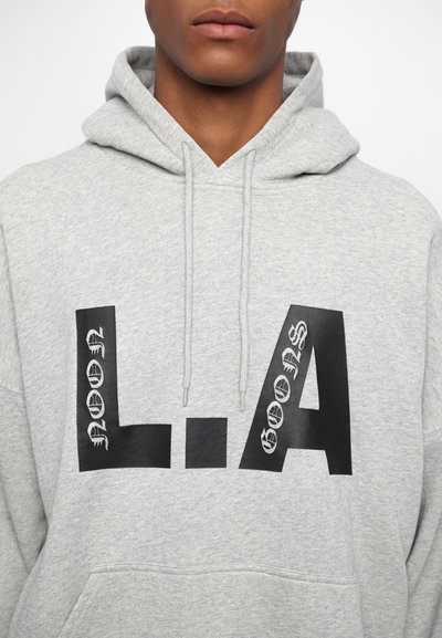 Grauer Kapuzenpullover mit einer Kängurutasche; verfügt über einen großen schwarzen "L.A"-Druck und zusätzliche schwarze Textdetails an den Seiten. Weiches Material, lässiges Design.