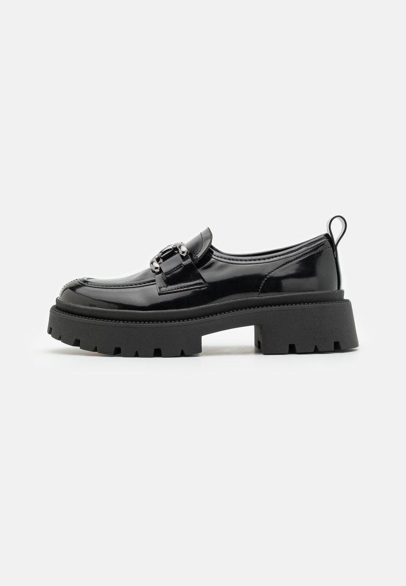Chaussure en cuir verni noir avec une semelle épaisse texturée, une bride décorative avec une boucle métallique et une languette à l'arrière du talon.