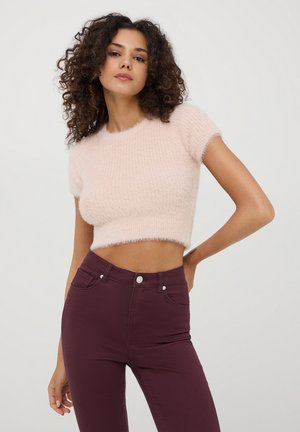Maglione corto di un delicato rosa realizzato in materiale morbido e peloso, con maniche corte. Abbinato a jeans bordeaux a vita alta con tasche frontali.