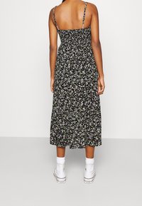 Svart blommig midiklänning med tunna axelband, en smockad överdel och en flödande kjol med små vita och gröna blomster mönster.