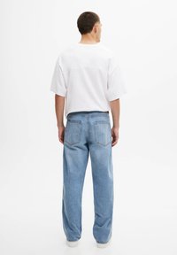 Bílý oversize tričko s nízko posazenými rameny v kombinaci se světle modrými širokými džíny s dvěma zadními kapsami a klasickým denimovým vzhledem.