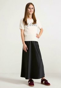 Knit ivory top with short sleeves featuring "Voila" in silver, paired with a long black satin skirt and burgundy sneakers.