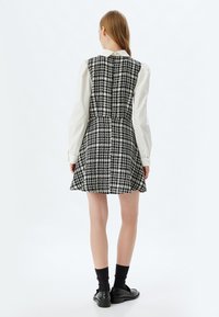 Vestido a cuadros en blanco y negro con cintura ajustada, falda acampanada y una camisa blanca con cuello debajo; cuenta con un cierre de cremallera en la parte posterior.