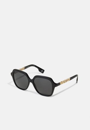 Gafas de sol negras de gran tamaño con montura cuadrada, lentes oscuros y detalles en tono dorado con el logotipo de "Burberry" en las patillas.