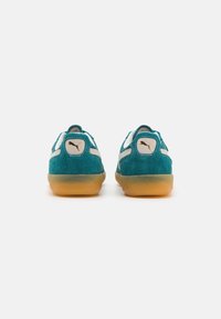 Puma sneakers in teal suede with white accents, rounded shape, and gum rubber soles. Features logo patches on the heel.