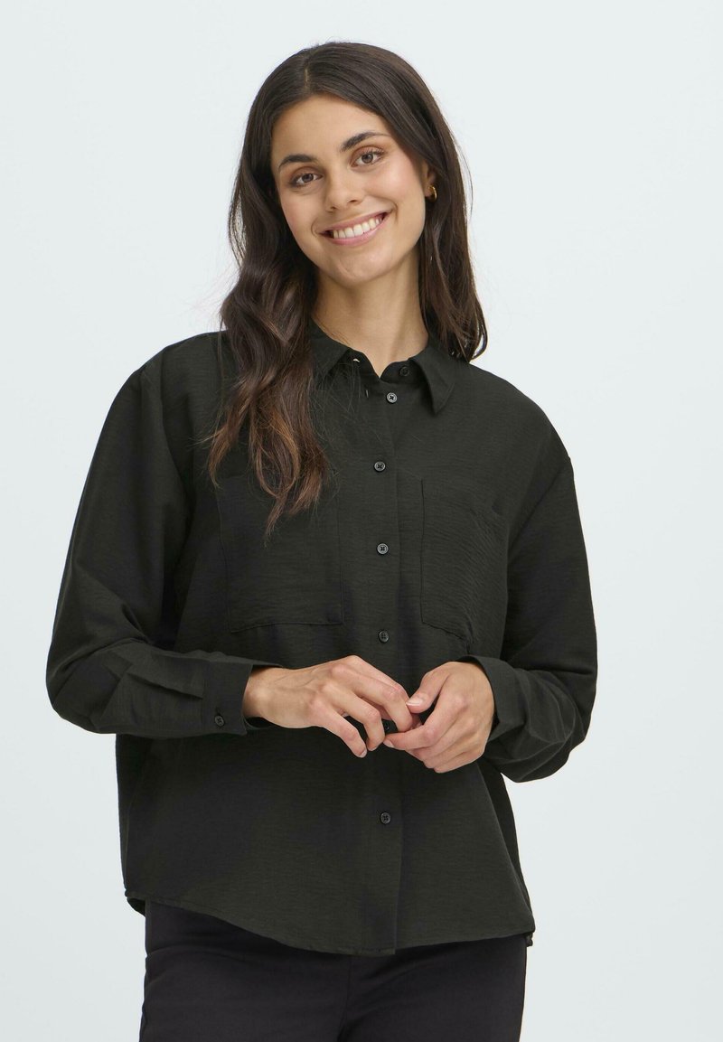 Black long-sleeve button-up shirt with a pocket, made of textured fabric. The shirt has a relaxed fit and a curved hemline.