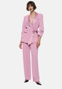 Blazer rosa con colletto in raso e pantaloni a gamba larga abbinati. Tessuto morbido, vita con cintura e due tasche sul blazer.