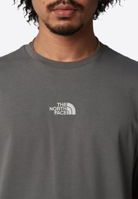 Šedé bavlněné tričko s logem The North Face, kulatým výstřihem a krátkými rukávy. Hladká textura, jednoduchý a klasický design.