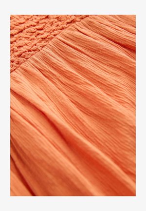 Persiko spalvos audinys, viršuje turintis tekstūruotą smulkintą dalį, pereinantį į švelniai susiraukšlėtą, laisvai krintantį medžiagą apačioje.