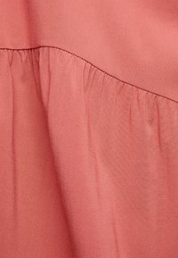 Tecido coral claro com uma textura suave, apresentando detalhes franzidos cozidos ao longo da costura, criando um design fluido.