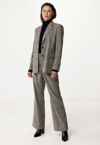 Plaid suit with a fitted blazer and wide-leg trousers, featuring a mix of gray, black, and brown. Worn with a black turtleneck and heeled boots.