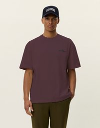Maroon oversized t-shirt with short sleeves, featuring a subtle logo in dark blue. Complemented by a blue cap with "LES DEUX" in white embroidery.