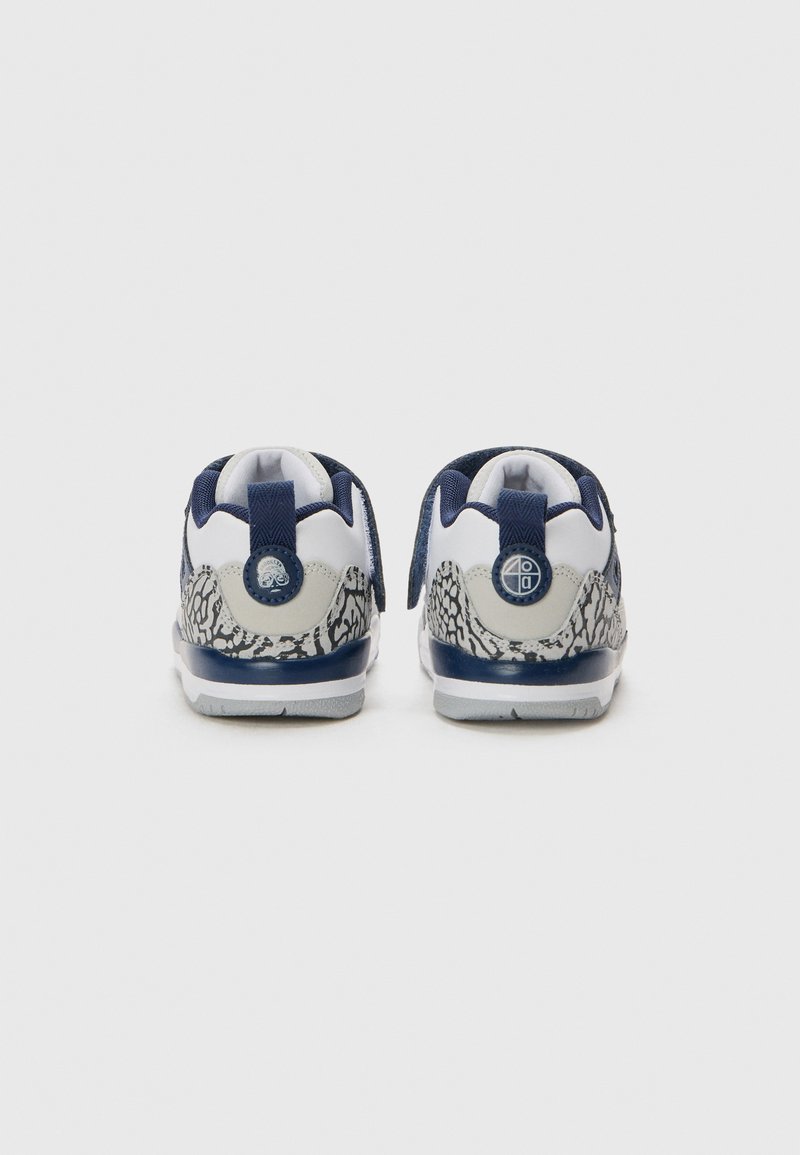 Zapatillas con una base blanca, acentos en azul marino y estampado animal gris. Presentan un cuello acolchado, una tira en el talón para facilitar el calzado y una suela texturizada para mayor agarre.