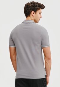 Szary polo wykonane z gładkiego materiału, z klasycznym kołnierzykiem oraz krótkimi rękawami z białymi paskami przy mankietach.