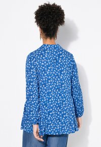 Blå långärmad blus med ett spritt hjärmönster i vitt och ljusblått, med en peplumdesign och elastiska ärmslut.