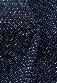 Marineblauwe textuurstof met een rasterpatroon gevormd door kleine witte stippen, wat een gestructureerd en visueel aantrekkelijk oppervlak creëert.