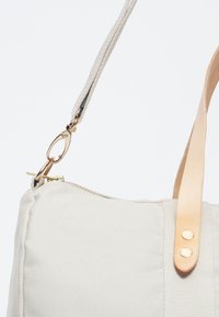 Borsa in tela beige chiaro con cerniera dorata, manico in pelle e chiusura metallica. Texture liscia con cuciture visibili e un design minimalista.