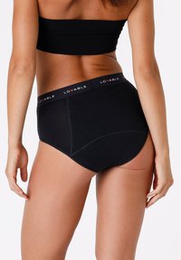 Slip in cotone nero con design a vita alta, caratterizzato da un elastico con logo e una consistenza morbida, mostrato da dietro.