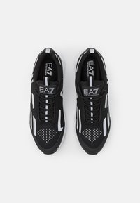 Par av svarta och vita EA7 Emporio Armani sneakers med snörningsdesign och märkeslogotyp på tungan, sedd ovanifrån på en vit bakgrund.
