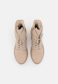 Un paio di stivali in suede beige con lacci, zip laterali e foderati in pelliccia, mostrati dall'alto su uno sfondo bianco.