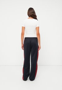 Witte fitted t-shirt met korte mouwen, gecombineerd met marineblauwe sweatpants met rode zijstrepen en een elastische tailleband, gezien vanuit de achterkant.